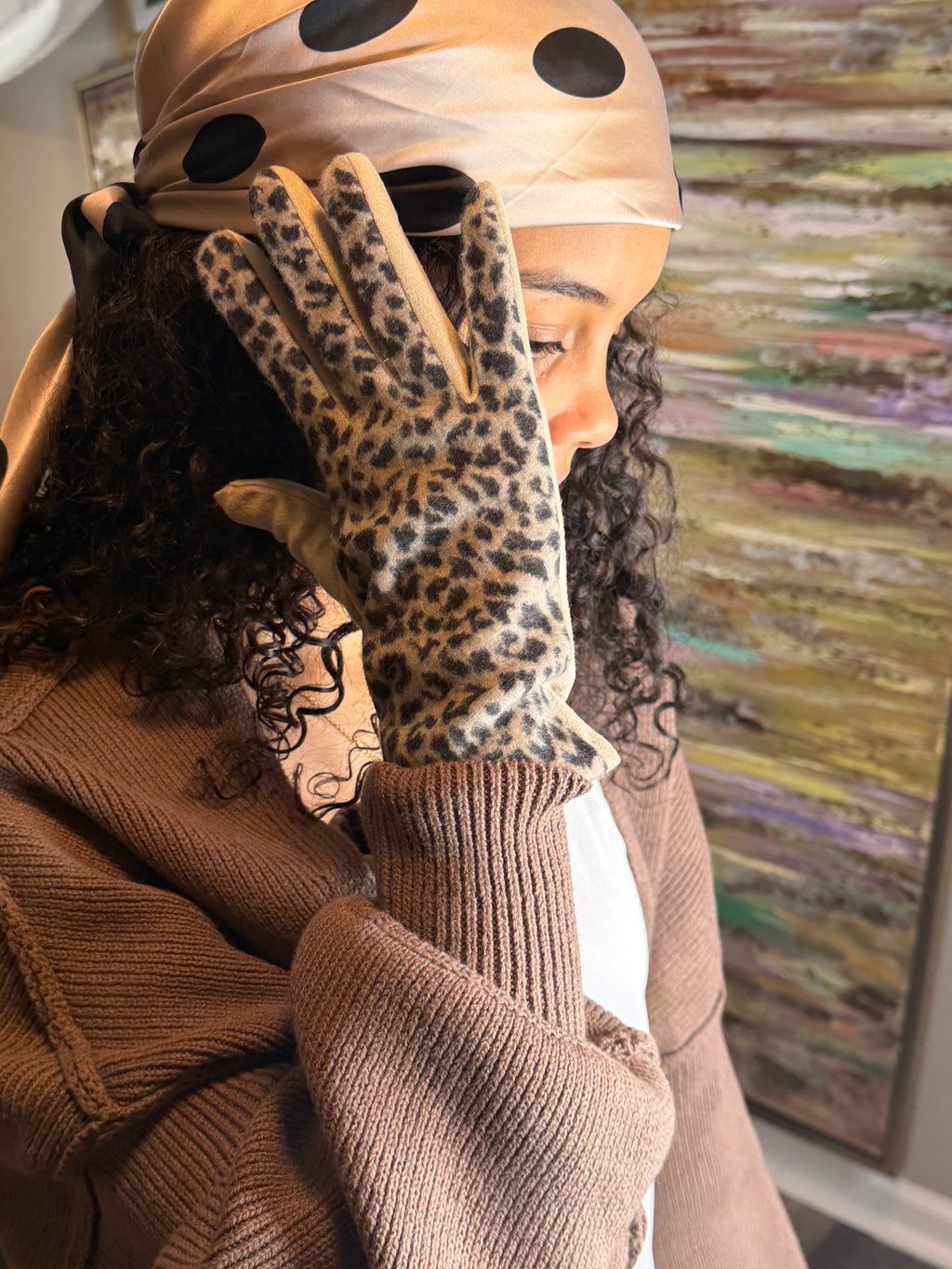 Person wearing leopard print gloves with a colorful abstract painting in the background