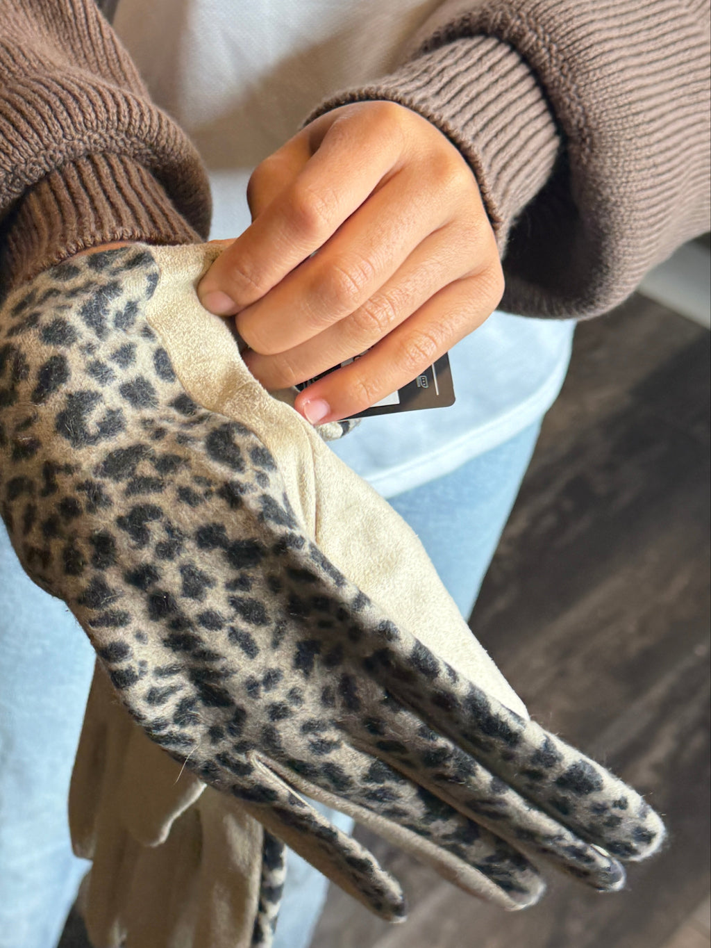Person wearing a brown sweater and leopard print gloves sitting on a wooden floor.