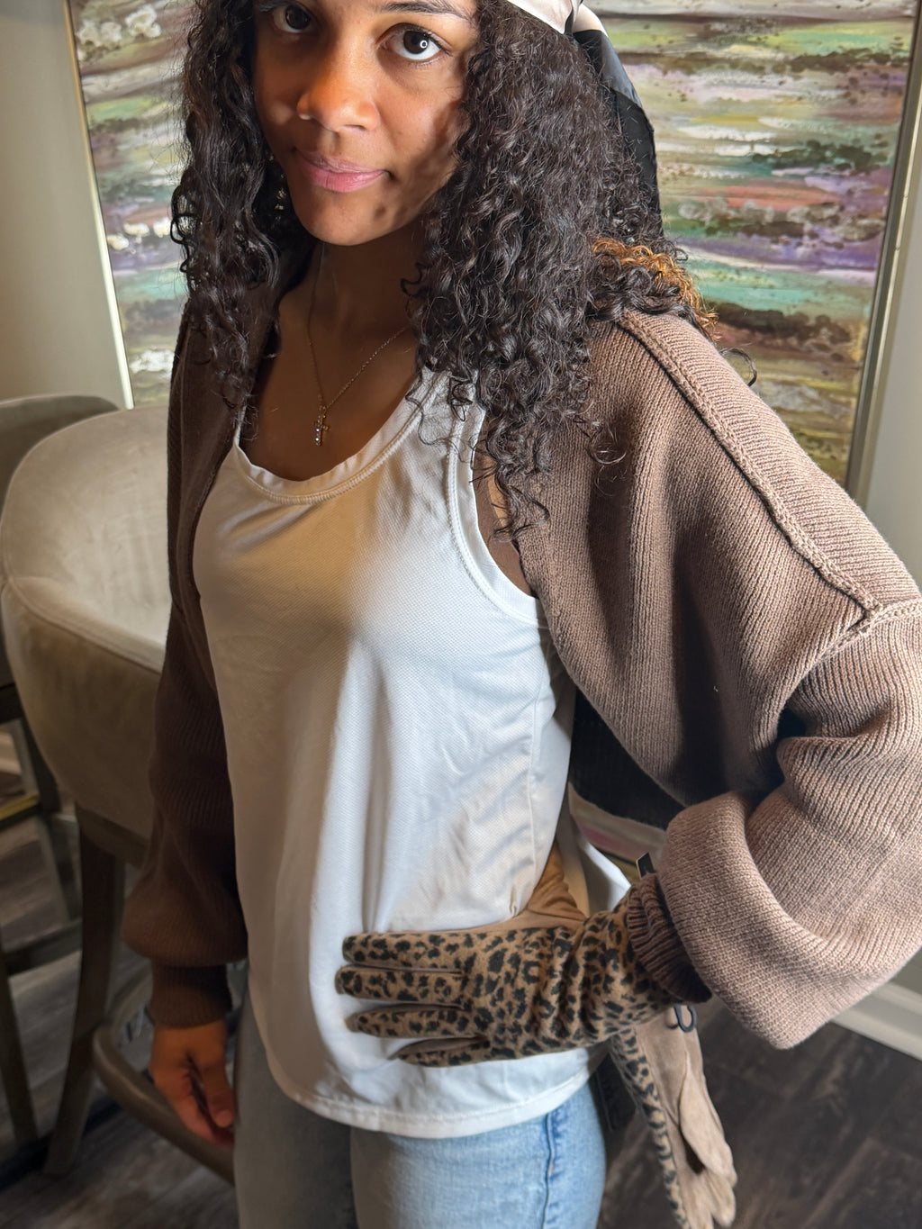 Woman sitting on a couch wearing a brown cardigan and leopard print gloves.