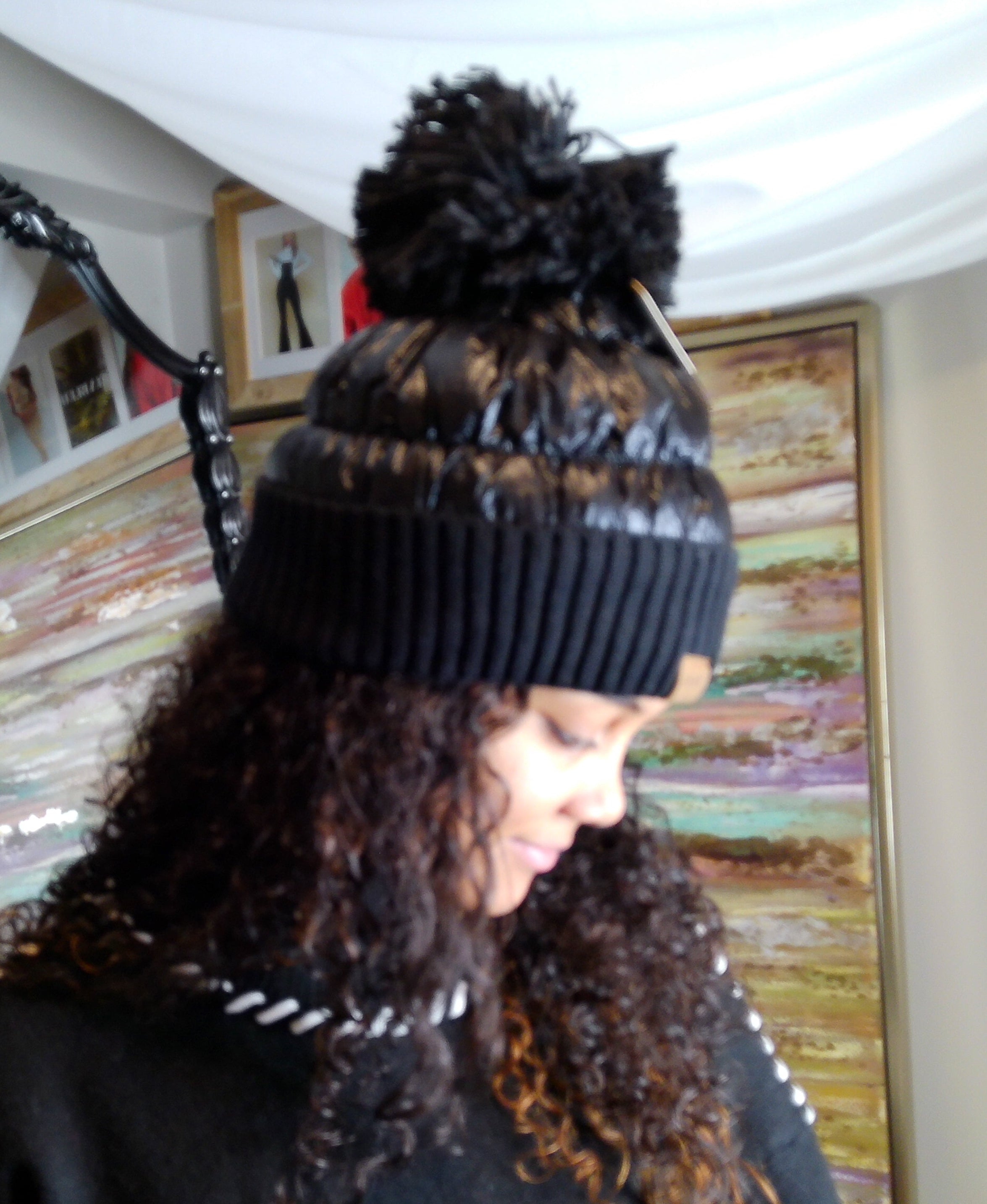 Person wearing a black beanie with a pom-pom indoors.